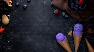 블루베리 맛 아이스크림 콘, 토핑 및 검은 책상 배경에 복사 공간이 있는 여름 디저트의 상위 뷰