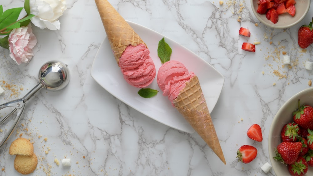 Top view of summer dessert with strawberry flavour ice-cream cones and topping on marble desk background