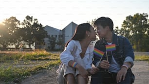 LGBT lesbian couple looking at each other face and smiling while sitting at the evening parks/outdoor with beautiful sunny and building as background.