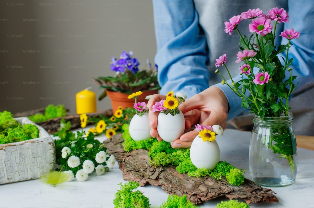 Woman preparing Easter decoration with eggs and flowers inside it on pine bark. Tutorial how to make festive composition for Easter table. Step 3.