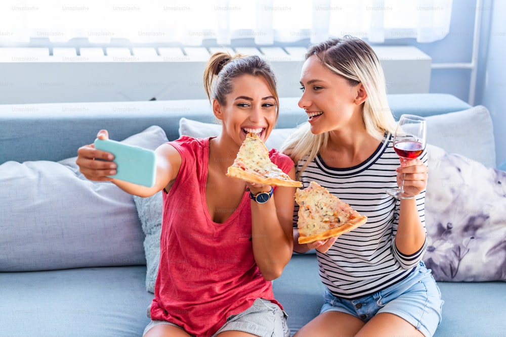 피자를 먹고 셀카를 위해 웃는 친구들. 그들은 피자를 공유하고 모바일 스마트 폰에서 셀카 사진을 만들고 있습니다. 그들은 집에서 파티를하고 피자를 먹고 재미있게 놀고 있습니다.
