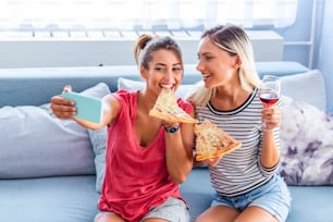 Freunde essen Pizza und lächeln für Selfies. Sie teilen Pizza und machen Selfie-Fotos auf dem mobilen Smartphone. Sie feiern zu Hause, essen Pizza und haben Spaß.