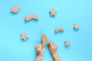 Wooden toys concept. Child playing with wooden toys galaxy on blue background. Top view, flat lay.