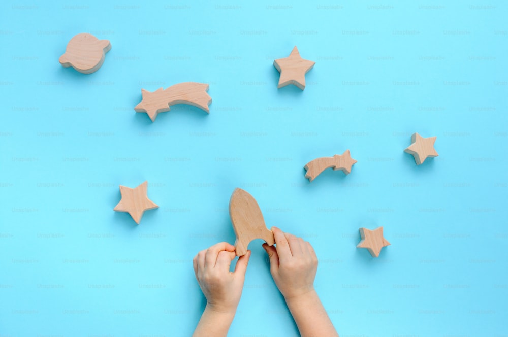 Wooden toys concept. Child playing with wooden toys galaxy on blue background. Top view, flat lay.