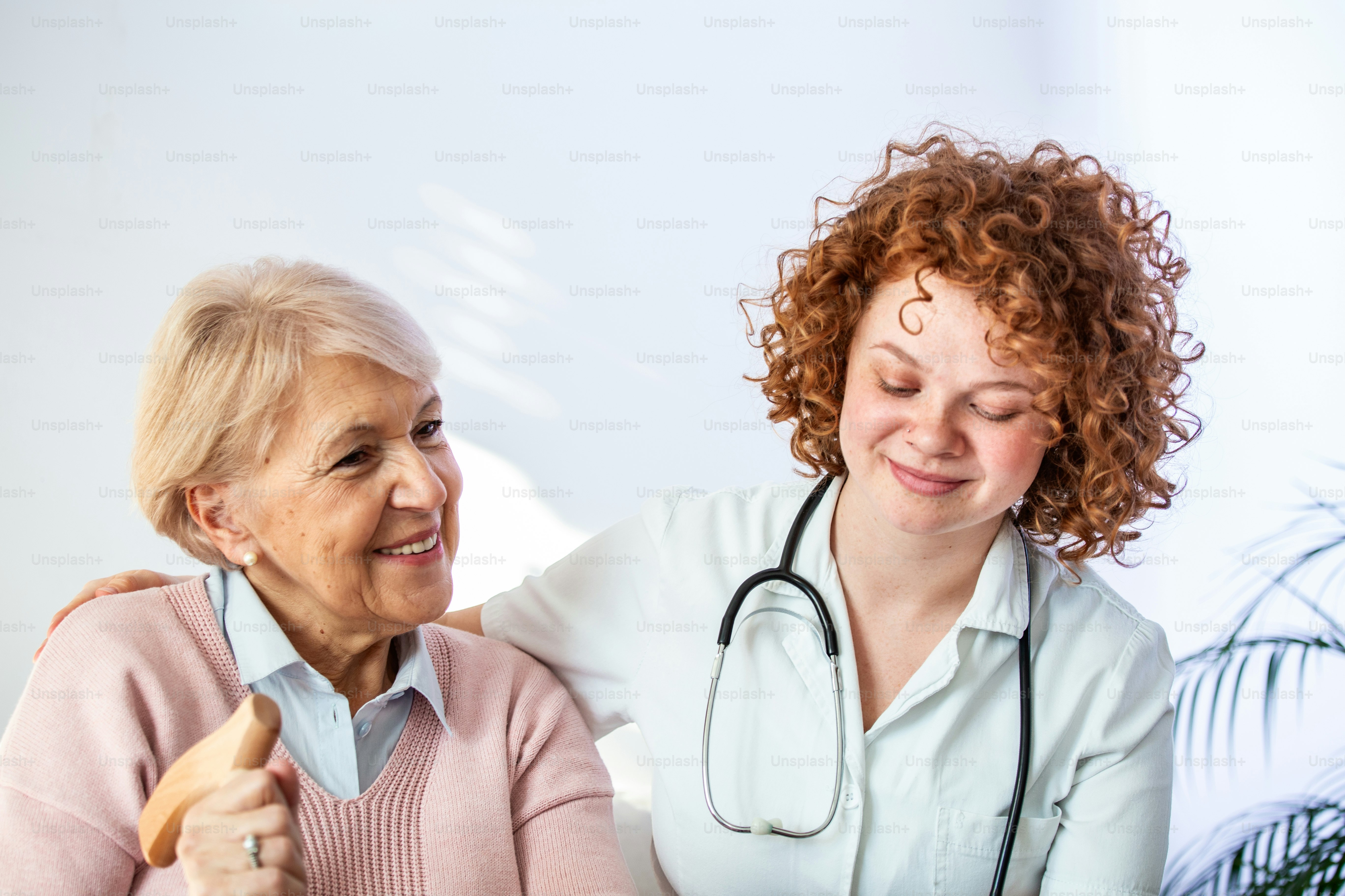 Happy patient is holding caregiver for a hand while spending time together. Elderly woman in nursing home and nurse. Aged elegant woman at nursing home