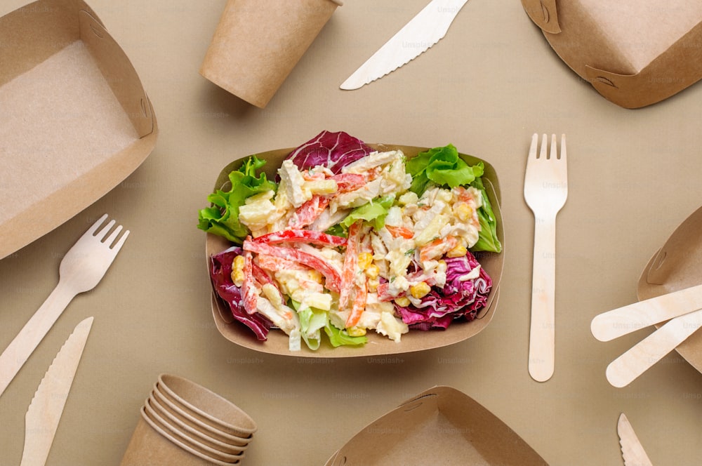 Disposable eco friendly food packaging. Vegetable salad in the brown kraft paper food container on beige background. Top view, flat lay.
