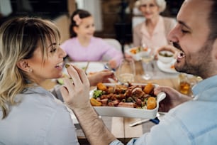 Happy man having fun while feeding his wife during family lunch at dining table.