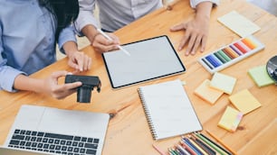 Cropped shot of young designer team sitting at the wooden working desk while holding camera in hands and discussing about information in tablet. Brainstorming/discussing/meeting of designer concept.