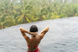 Back view of a slim young female with her hands behind her head bathing outdoors