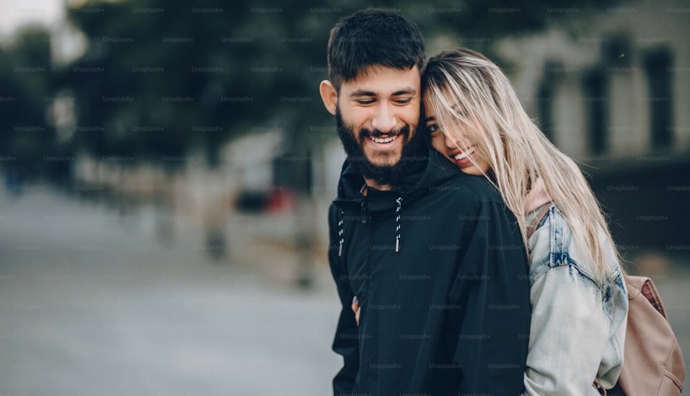 Handsome bearded boy being embraced by his caucasian blonde girl while walking and smiling cheerfully