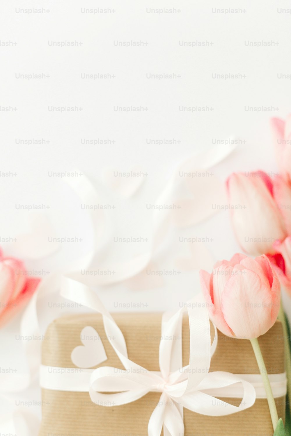 Tulipes roses avec ruban et boîte cadeau sur fond blanc, mise à plat. Image verticale élégante. Bonne journée de la femme. Carte de vœux avec espace pour le texte. Bonne fête des mères. Maquette de mariage ou de Saint-Valentin