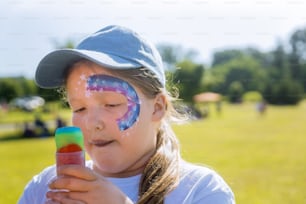 Teenager with face paint eating rainbowl color ice cream.