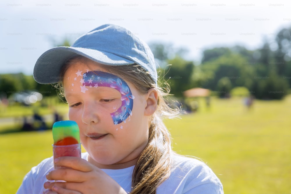 Teenager with face paint eating rainbowl color ice cream.