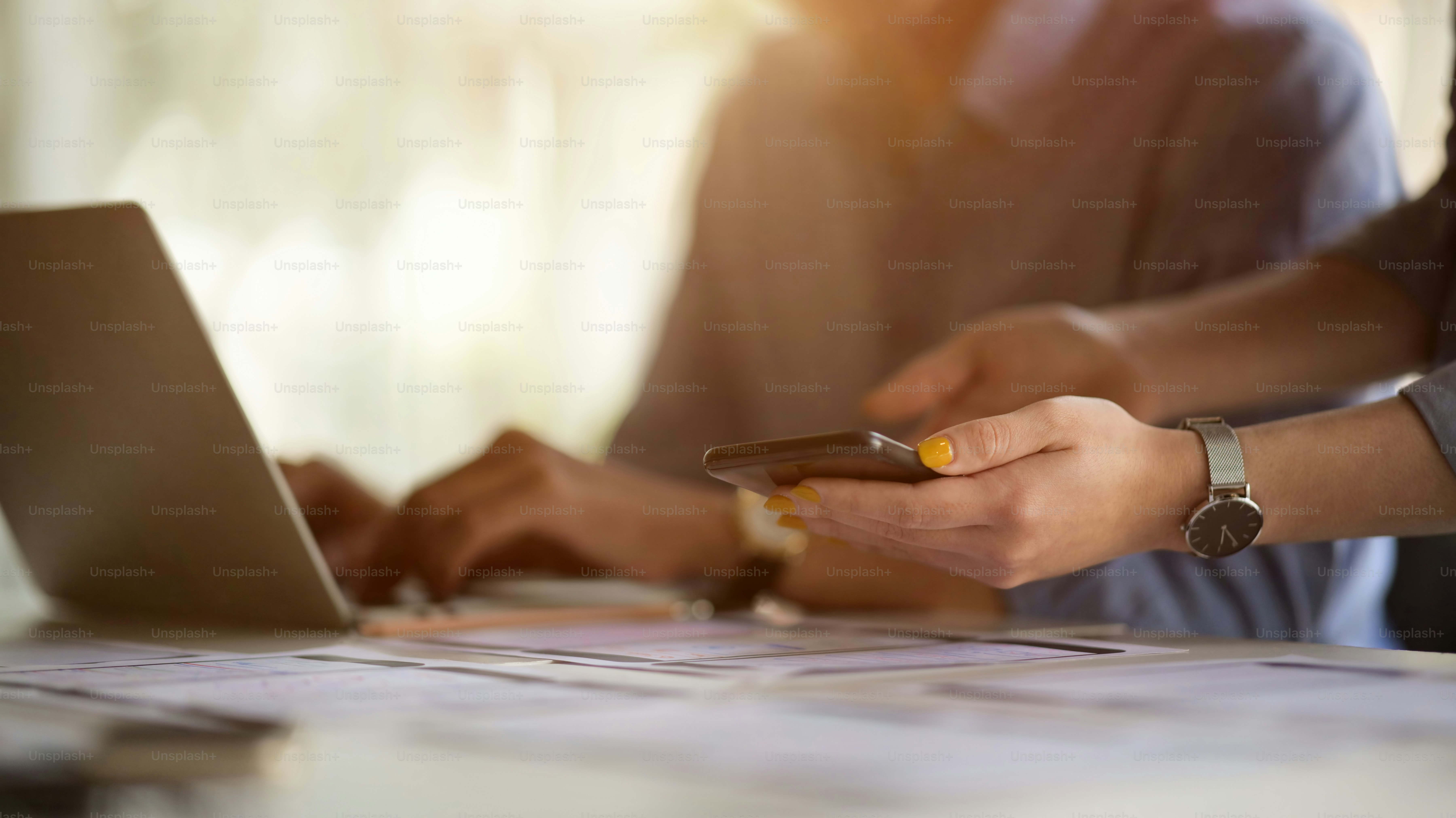 Cropped shot of professional UI developer team briefing on their project with smartphone and laptop in simple office room