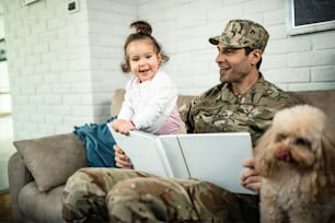 행복한 군인 아버지와 그의 딸이 사진 앨범을보고 집에서 즐거운 시간을 보내고 있습니다.