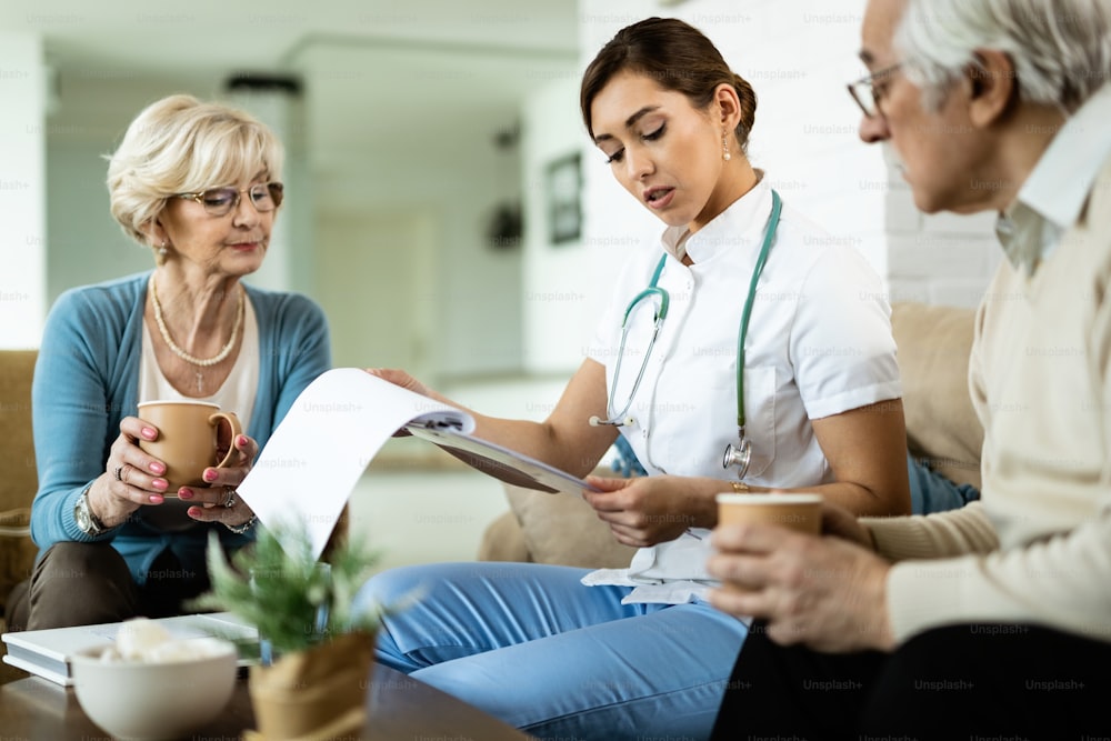 Un jeune travailleur de la santé et un couple de personnes âgées analysant les résultats des tests médicaux lors d’une visite à domicile.