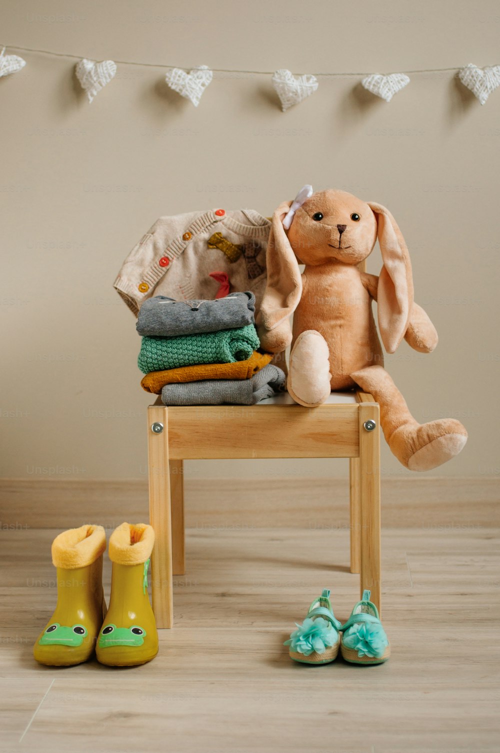 Baby girl clothing and shoes, rabbit toy on the wooden chair in children room. Selective focus.