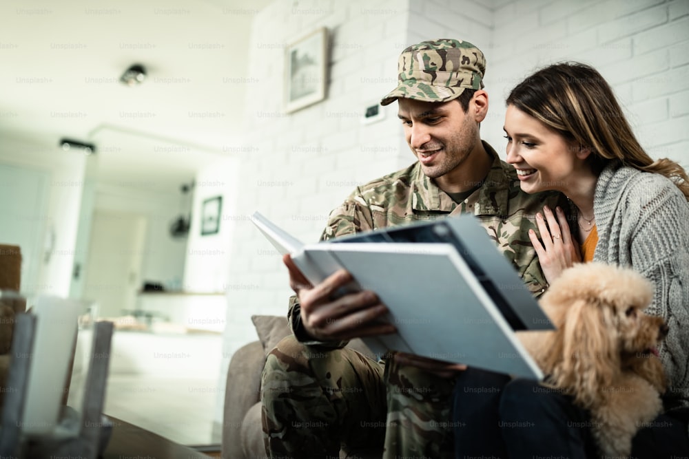 Happy army soldier and his wife looking at their photo album while relaxing at home.