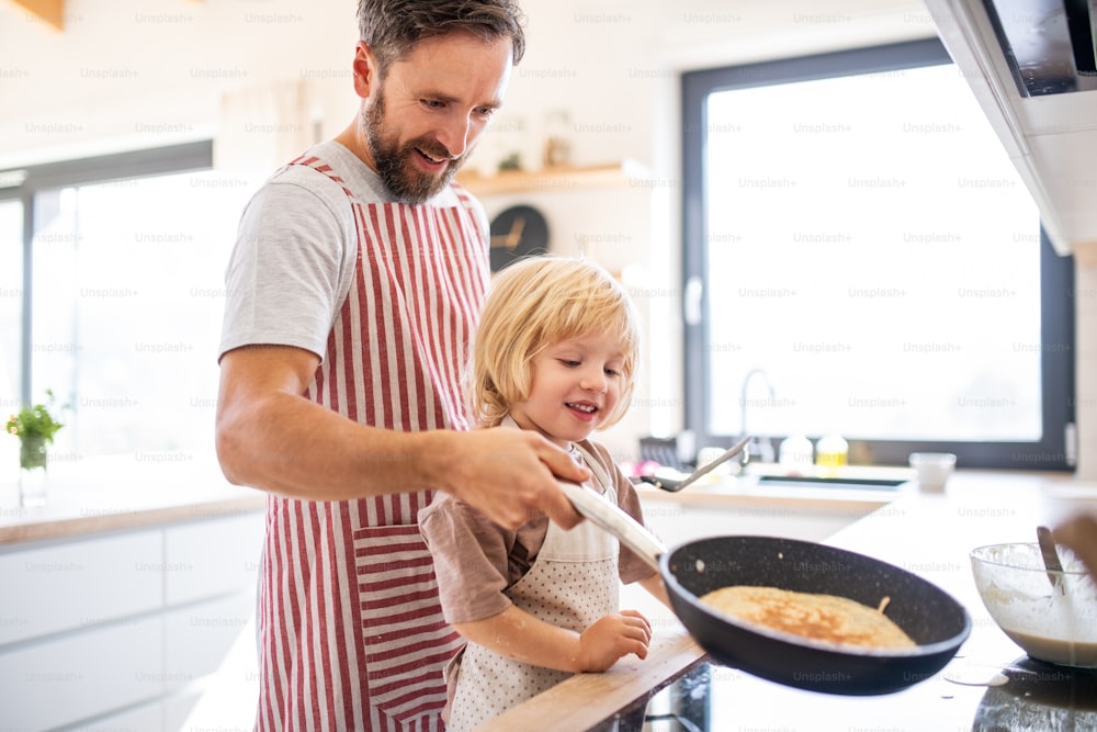 Une vue latérale d’un petit garçon aidant son père à l’intérieur dans la cuisine à faire des crêpes.