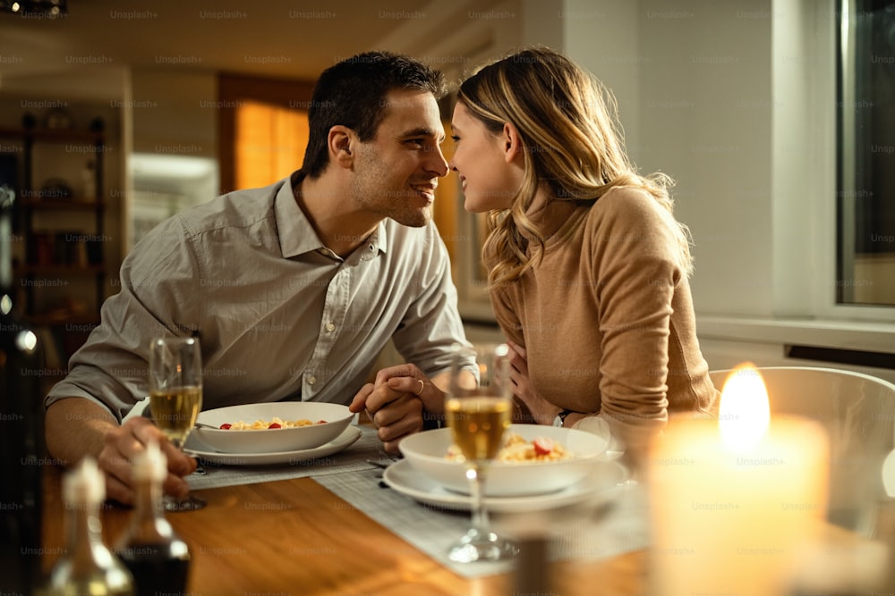 Pareja romántica a punto de besarse mientras se toman de la mano durante la cena en la mesa del comedor.