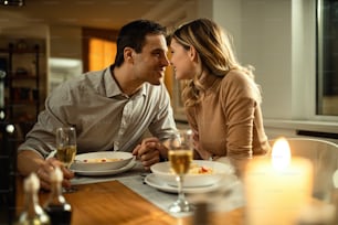 Romantisches Paar, das sich küsst, während es während des Abendessens am Esstisch Händchen hält.