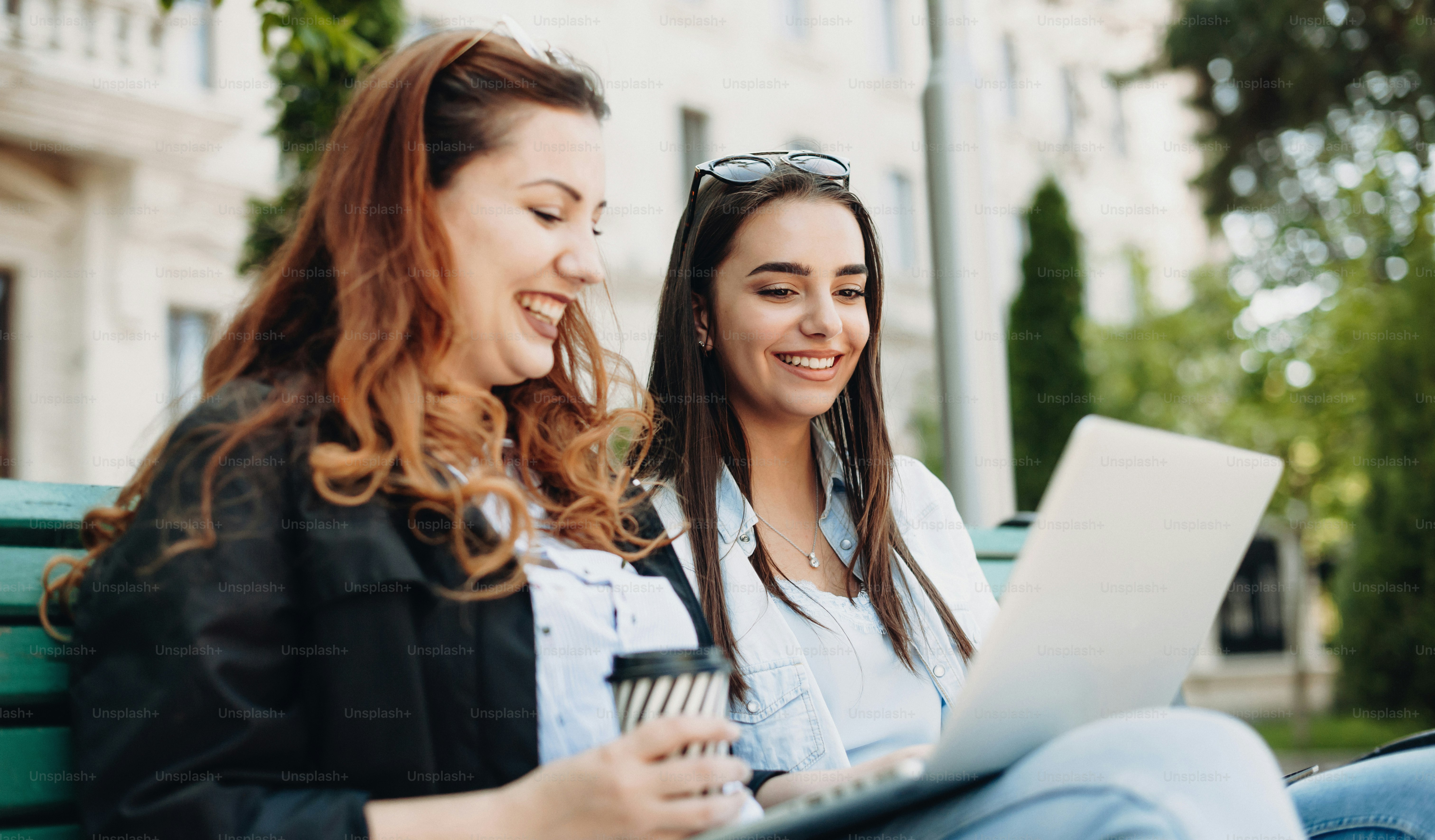 Plus sized caucasian businesswoman having a break near her brunette coleague on a bench in park holding a pc