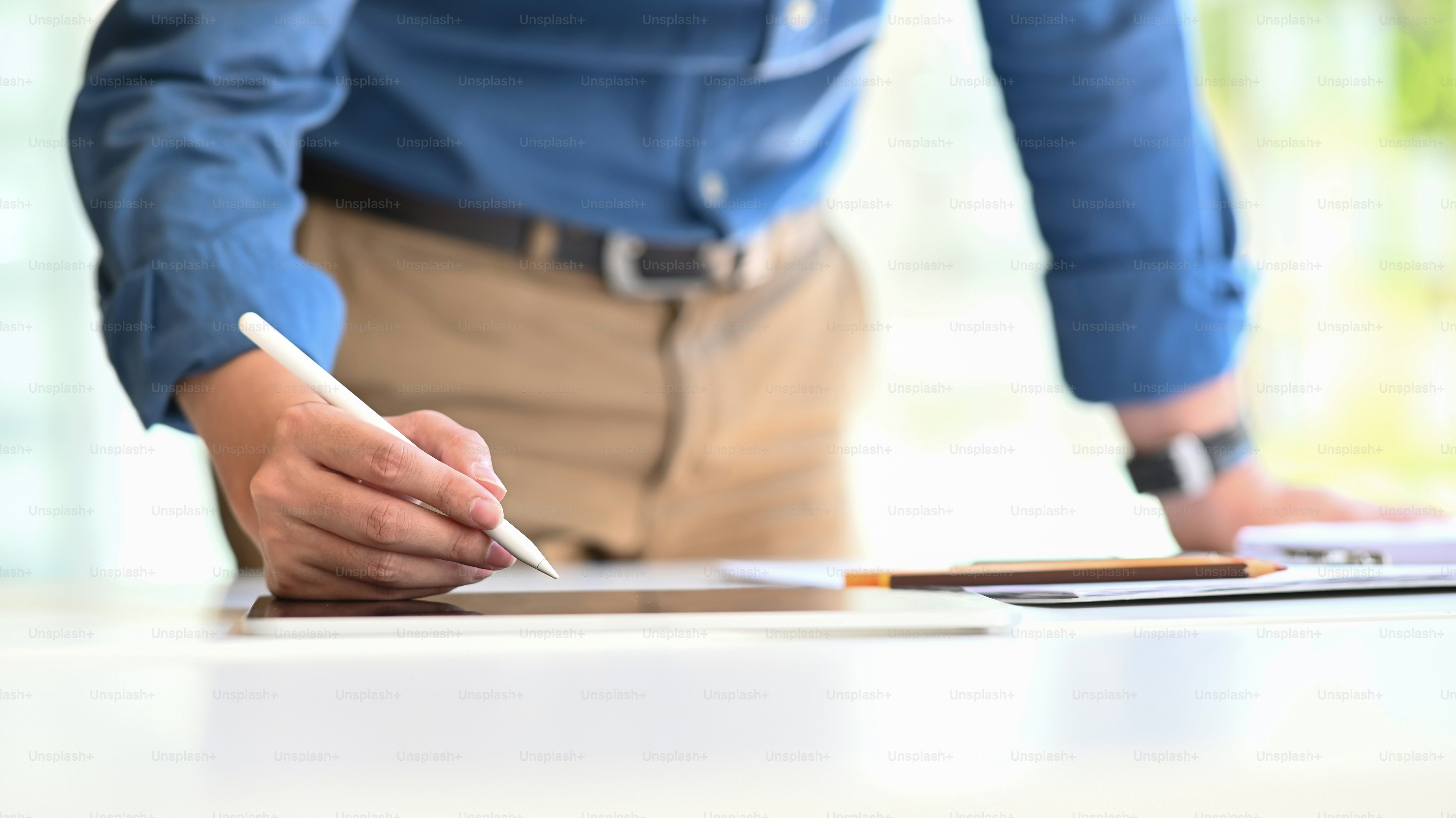 Hombre creativo que trabaja como arquitecto de pie y escribe/dibuja en la tableta de la computadora que pone en la mesa de trabajo moderna con el fondo cómodo de la oficina.