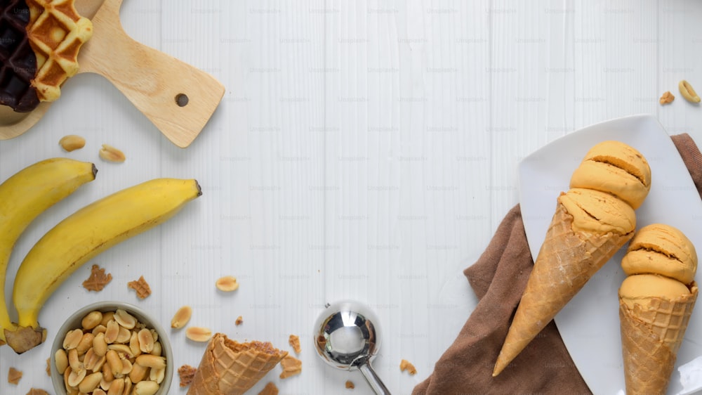 Vue aérienne d’un dessert d’été avec des cornets de crème glacée au beurre de cacahuète à saveur de banane, une gaufre, une garniture et un espace de copie sur fond de bureau en planches