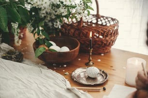 Pâques élégant Rural nature morte. Oeuf de Pâques élégant avec des ornements de cire modernes et des œufs teints naturels sur une table en bois rustique avec des fleurs de printemps, un panier, une bougie, une toile de lin.  Zéro déchet