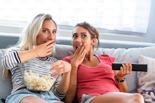 Portrait of a happy girlfriends eating popcorn and watching tv at home. Girls night, entertainment and junk food concept watching tv and movies