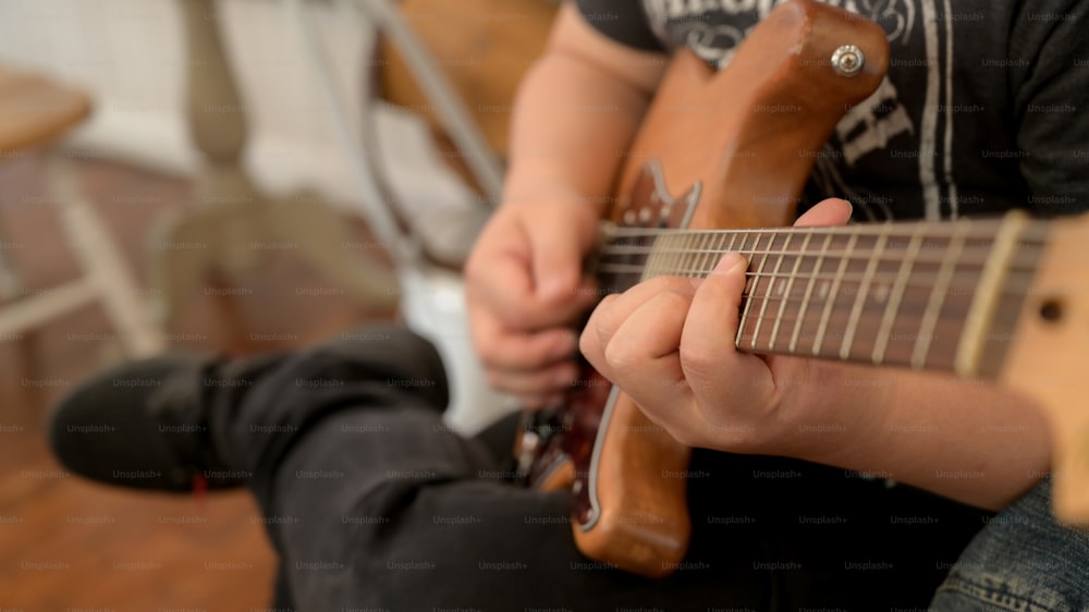 Colpo ritagliato di musicista maschio che si esercita con la chitarra mentre si siede sulla sedia in uno strumento musicale