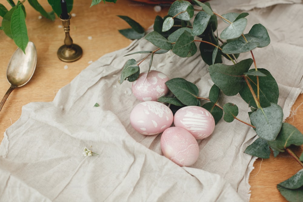 Uova di Pasqua moderne con ramo di eucalipto su tavolo rustico in legno. Eleganti uova di Pasqua rosa pastello con ornamenti floreali dipinti in tintura naturale di barbabietole. Cartolina di auguri di buona Pasqua