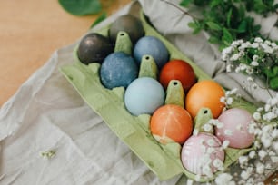 Modern yellow, pink, blue and grey easter eggs painted with organic onion, beets, red cabbage, carcade tea. Zero waste holiday. Natural dye easter eggs in carton tray on rustic table with flowers