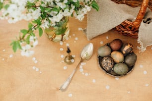 ハッピーイースターフラットレイ。バスケット付きの素朴な木製のテーブルに春の花が咲いたモダンなイースターエッグ。スタイリッシュなグレーの石と緑のイースターエッグは、カーケードティーの天然染料で描かれています。