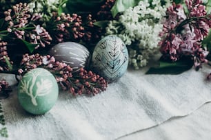 happy easter. easter eggs with floral and chick ornaments on rustic background with lilac flowers. top view. space for text.  greeting card concept. stylish decoration