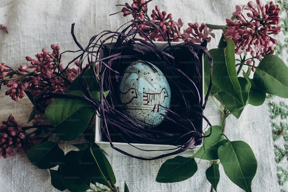 Huevo de Pascua en nido con adornos florales y de polluelo sobre fondo rústico con flores lilas. Vista superior. espacio para el texto. Felices Pascuas. concepto de tarjeta de felicitación. Decoración con estilo