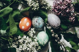 Ostereier mit lila Blüten auf rustikalem Hintergrund und Muschiweide. Grußkartenkonzept. Draufsicht. bunt dekoriertes Ei mit Blumen- und Hühnerornamenten. Frühlingsferien. frohe Ostern
