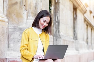 Beautiful asian woman using laptop computer. Smiling asian girl sitting on stairs and using a laptop. Asian business woman using laptop computer