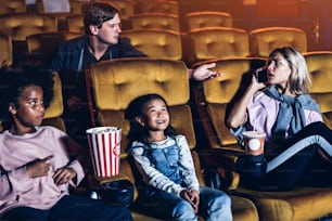 Caucasian woman talking on phone in the cinema and showing a rude gesture at the man behind her