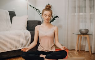 Red haired caucasian woman meditating on a red carpet on the floor in her dormitory before starting some stretching exercises