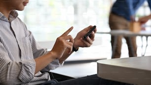 Un uomo d'affari seduto e utilizzando lo smartphone durante il lavoro in un ufficio moderno.