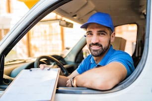 Portrait of a delivery man in van and giving clipboard to customer for signature. Delivery and shipping concept.