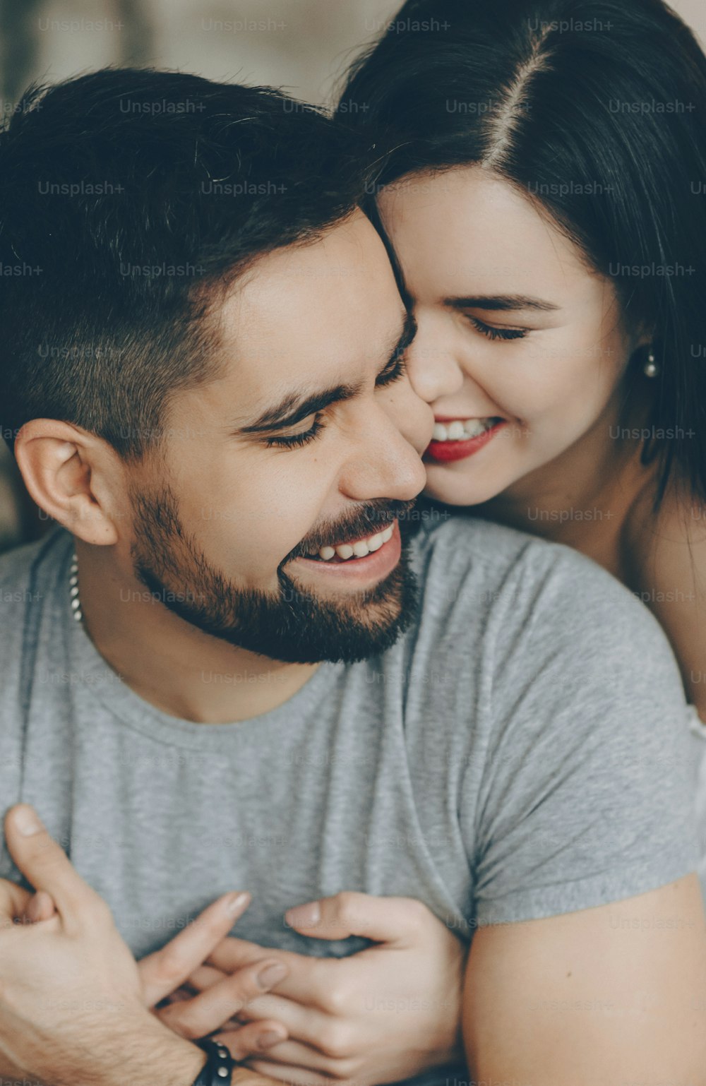 Cheerful caucasian brunette is embracing her bearded lover while smiling and having fun together