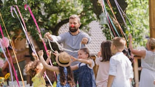 Man with group of kids on birthday party playing outdoors in garden in summer, celebration concept.