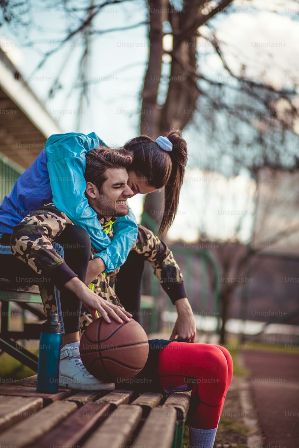 In love and in sport everything is allowed. Young couple sitting on bench in the park with basketball.