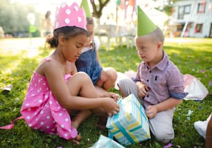 Niño con síndrome de Down con amigos en fiesta de cumpleaños al aire libre en el jardín, abriendo regalos.
