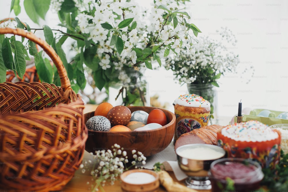 Easter eggs natural dyed, easter bread, ham, beets, butter, green branches and flowers on rustic wooden table with wicker basket and candle. Traditional Easter Food for blessing in church