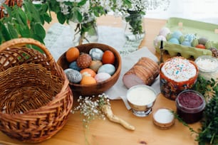 Easter modern eggs, easter bread, ham, beets, butter, green branches  and flowers on rustic wooden table with wicker basket and candle. Traditional Easter Food for blessing in church