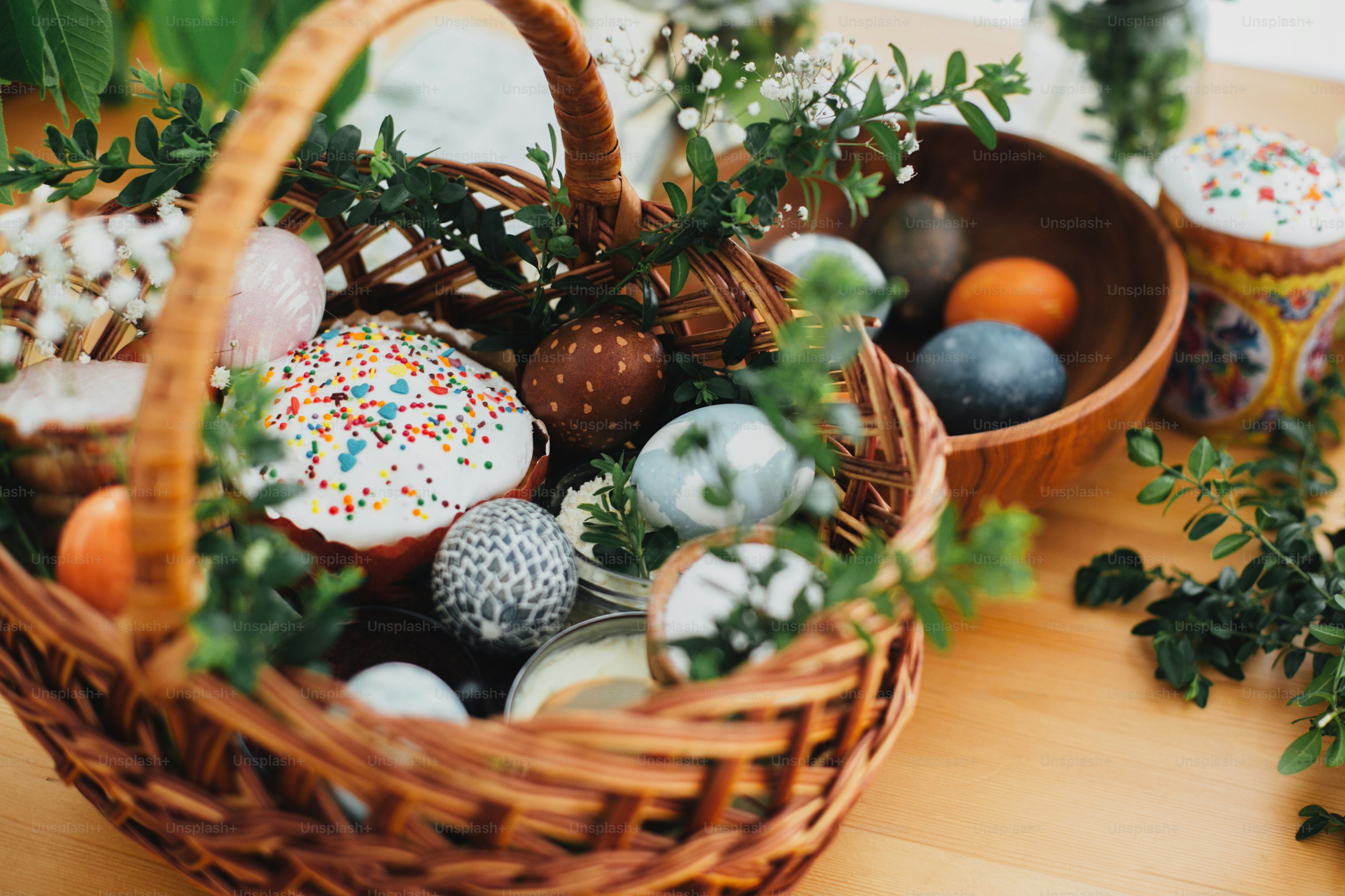 Traditioneller Osterkorb. Ostern moderne Eier, Osterbrot, Schinken, Rüben, Butter, im Weidenkorb verziert mit grünen Buchsbaumzweigen und Blumen auf rustikalem Holztisch
