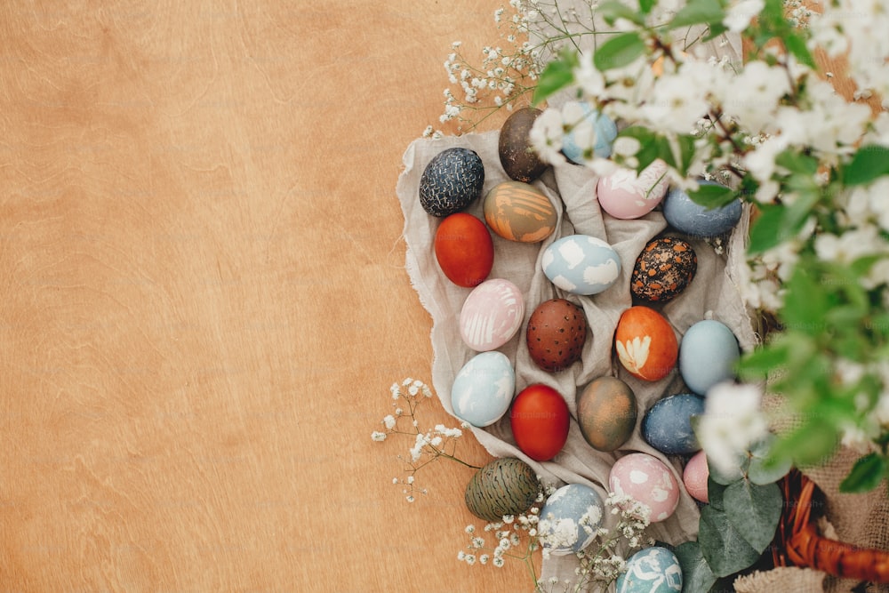 Buona Pasqua. Uova di Pasqua su sfondo rustico con fiori primaverili e rami verdi, flat lay rurale. Eleganti uova di Pasqua colorate con ornamenti moderni dipinti con tintura naturale. Spazio di copia